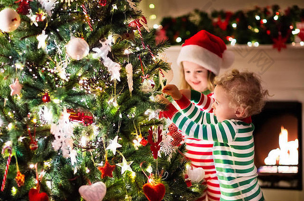 快乐的孩子们穿着红绿相间的条纹睡衣，在美丽的客厅里用火炉装饰圣诞树