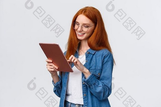腰身向上的肖像画：戴着眼镜的红头发的无忧无虑的欧洲女人，看着数码平板电脑，看起来很开心，很开心，很高兴