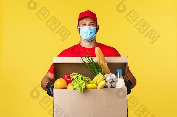 外卖，COVID-19检疫和食品杂货的概念。身着红色制服和医用口罩的快乐微笑信使将食品杂货箱带给顾客