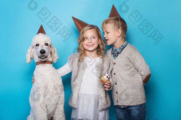 美丽的小女孩和英俊的男孩带着狗庆祝生日。友谊家庭蓝色背景上的工作室肖像