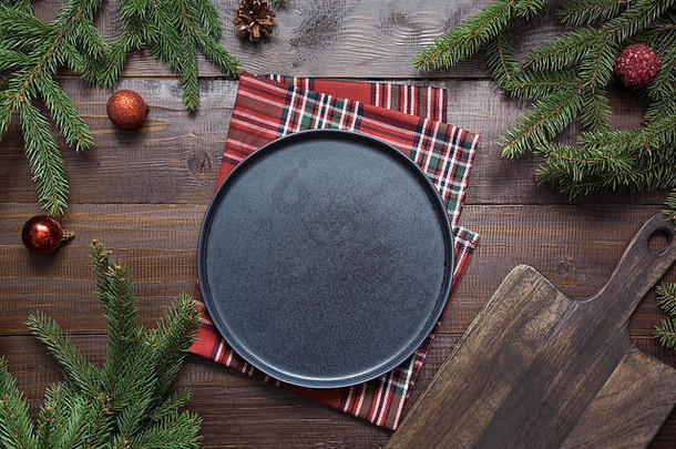 圣诞食品边框，黑色的盘子，绿色的树枝，红色的装饰在木板上。文本的空间。从上面看。