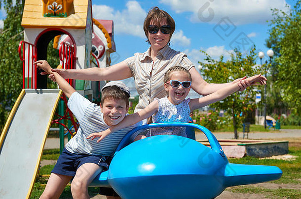儿童和妇女在城市公园的蓝色飞机上飞行，快乐家庭，暑假概念