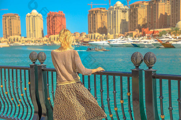 卡塔尔的旅游业。在码头走道上，一位金发碧眼的优雅女士注视着卡塔尔珍珠港——<strong>阿拉伯</strong>港。多哈的高加索游客