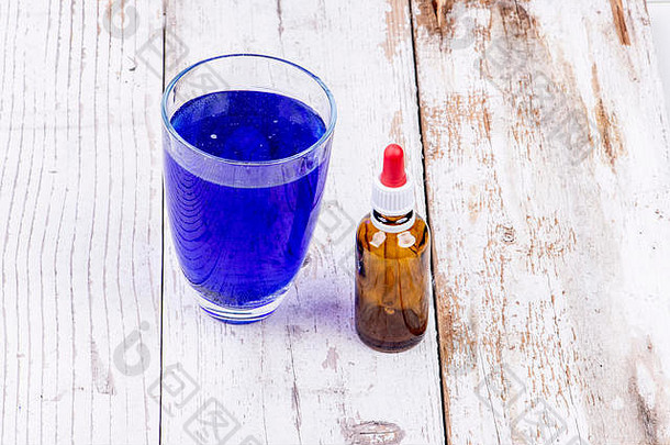 一个装有蓝色液体的玻璃杯，旁边是一个装有移液管的棕色药瓶