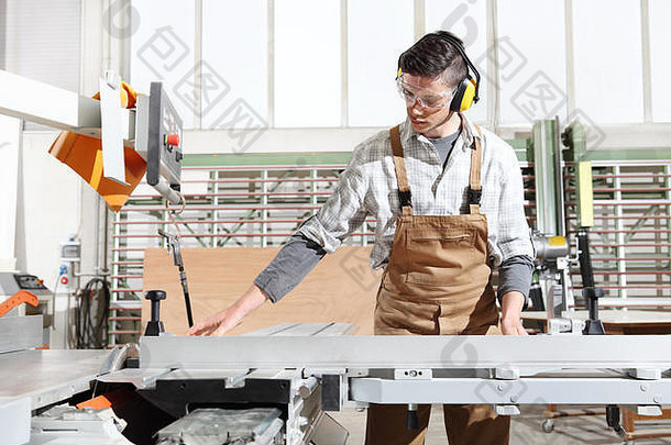 木工在细木工中工作，用圆锯机切割木板，用耳罩和眼镜保护