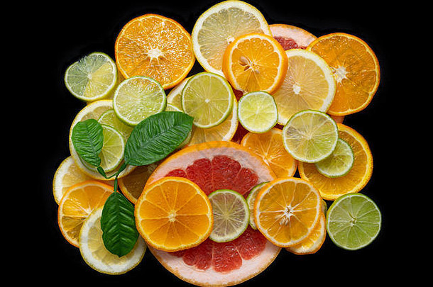 在黑色背景特写上分离的切片柑橘类水果，俯视图。多汁的成熟橙子、橘子、葡萄柚、酸橙和柠檬。水果混合物。