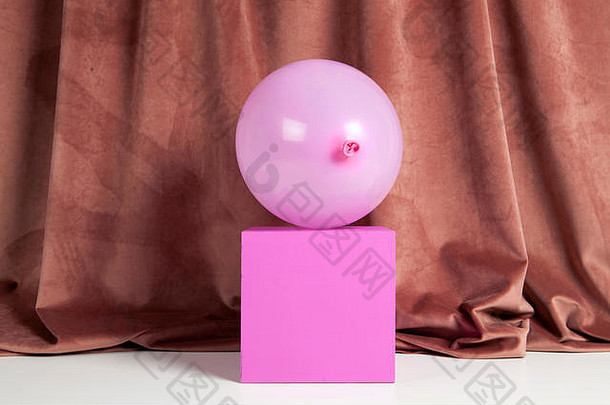 一个粉红色的充气气球，前面是一个粉红色的立方体，下面是一个粉红色的天鹅绒窗帘。色彩和谐。最小静物彩色摄影