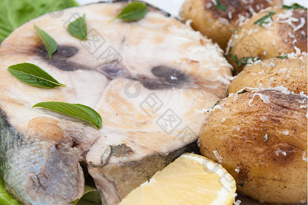 炸<strong>红金鱼</strong>牛排配柠檬片和烤土豆，白色盘子特写。