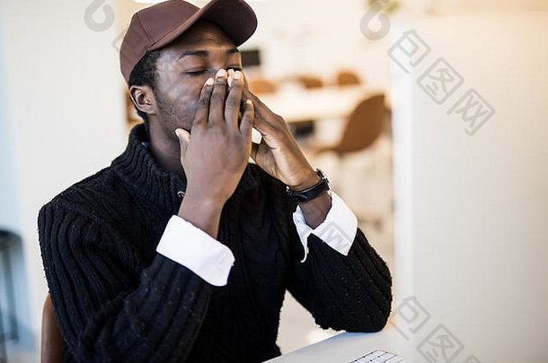 一位身穿西装的年轻非洲裔美国商人在办公室工作时感冒打喷嚏，这位黑人沮丧的雇员得了流感