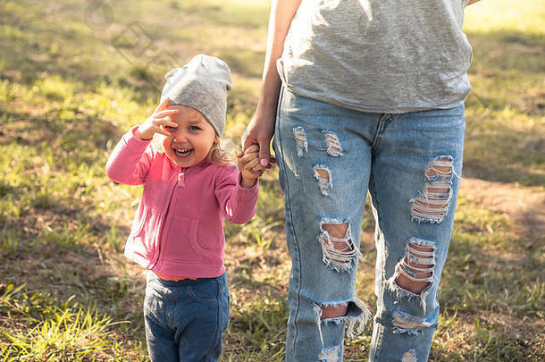 顽皮的孩子和妈妈手牵着手在夏季公园的草地上散步。主题是儿童。照片上是一位面目全非的母亲。概念