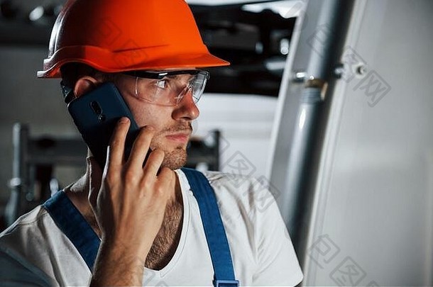 使用电话。冶金厂戴防护头盔和眼镜的工程师肖像
