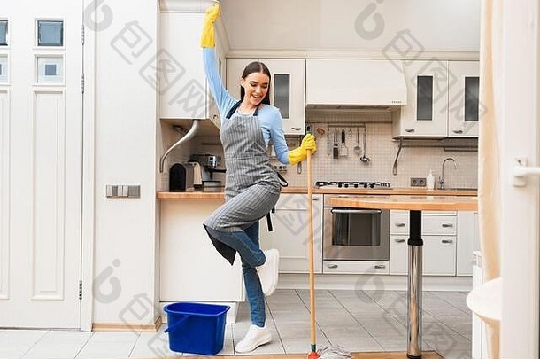 快乐的年轻女子用拖把舞动着清洁厨房地板