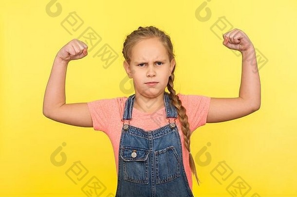 我很强壮！一幅勇敢的小女孩的画像，她梳着辫子，穿着牛仔工作服，举手展示肱二头肌，感受力量和信心，以<strong>健康成长</strong>。ind