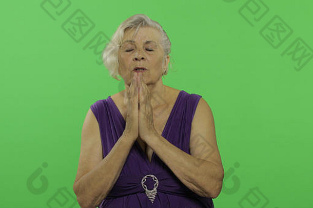 上了年纪的女人祈祷手紧握漂亮的祖母紫色的衣服的地方标志文本浓度关键绿色屏幕背景