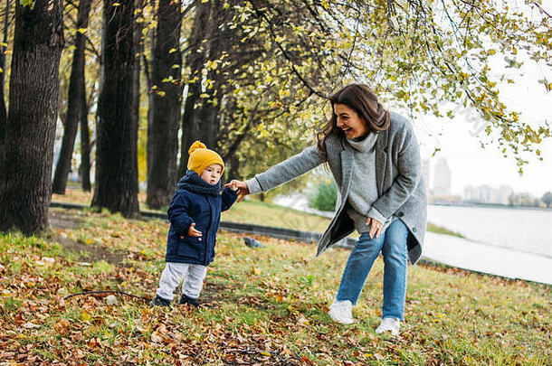 穿着时尚休闲服的可爱在秋季自然公园与母亲一起探索世界