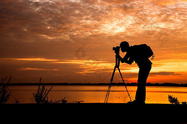 剪影英俊的摄影师在日落时用专业相机拍照。
