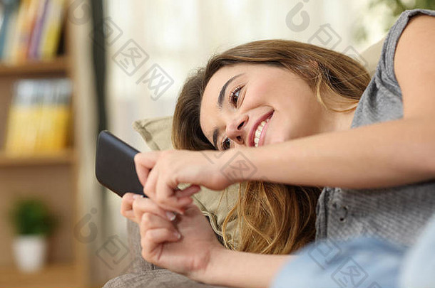 一个快乐的少年躺在家客厅的沙发上，用智能手机在线阅读文字