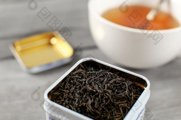 金属罐中的红茶，背景是一杯模糊不清的热琥珀饮料。