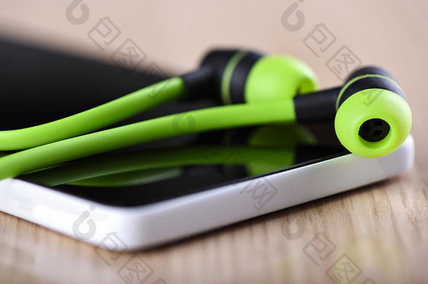 智能手机屏幕上的绿色耳机。耳机在智能手机屏幕上的反射。关注耳机