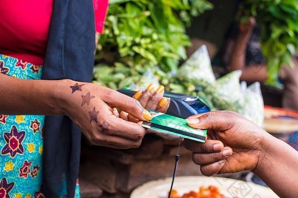 特写镜头：一名非洲妇女手持移动销售点设备在当地非洲市场上销售，从一名客户那里领取