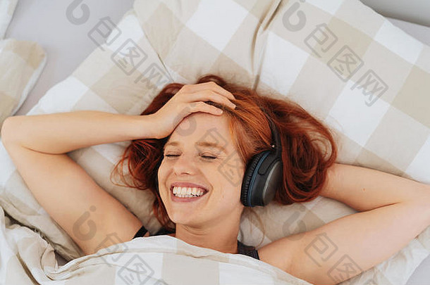 躺在床上用<strong>立体</strong>声耳机听音乐的年轻女子带着幸福的<strong>微</strong>笑