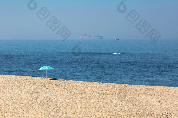 海滩风景：干净的沙滩、沙滩阳伞、海滩上的隔离物、毛巾、海浪、船和船、海鸥为背景的天空、葡萄牙