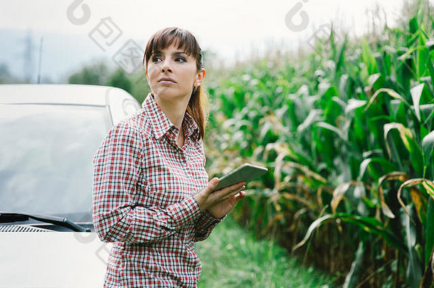 一个年轻悲伤的女人靠在她的车上，她在乡下迷路了，她正在用她的数字平板电脑寻找方向