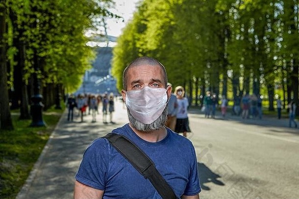 在冠状病毒感染CVID-19期间，在公共公园散步。一位留着胡子的中年男子在夏日傍晚散步时戴着口罩。