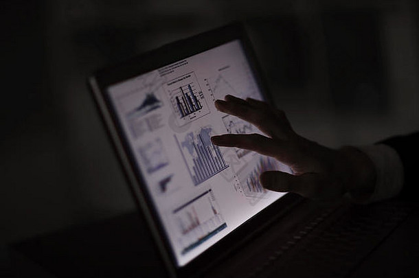 闭合。商人用手指着笔记本电脑屏幕上的财务图表