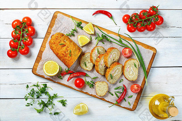 美味的烤箱烤鱼块，在案板上切成片，配以葱、欧芹、柠檬、辣椒、橄榄油和新鲜番茄