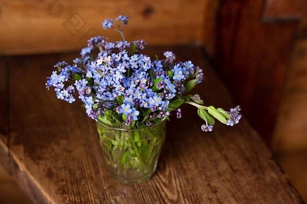 木制背景上玻璃杯中的蓝色野花。别忘了我。