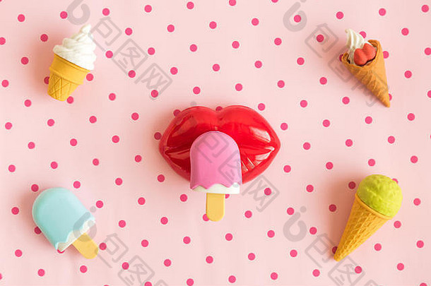 平铺的微型冰淇淋和塑料嘴唇，在柔和的粉红色波尔卡设计背景下隔离，最小限度的创意概念。
