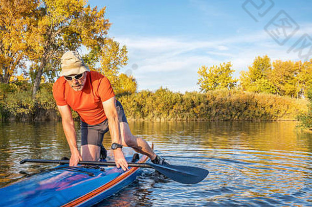这位资深男子桨手正在科罗拉多州的湖面上，以秋天的颜色，在他的竞速直立式桨板上开始训练