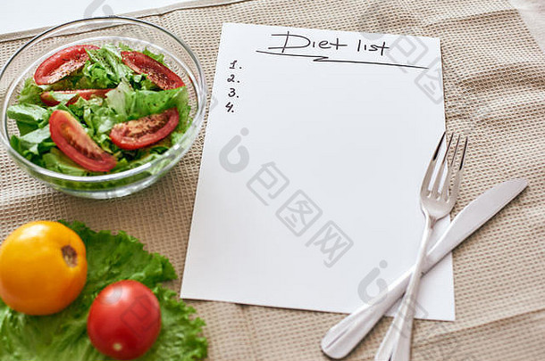 饮食清单。准备写食谱。桌上放着笔记本、桌布、叉子和刀。桌上有新鲜蔬菜。裁剪照片