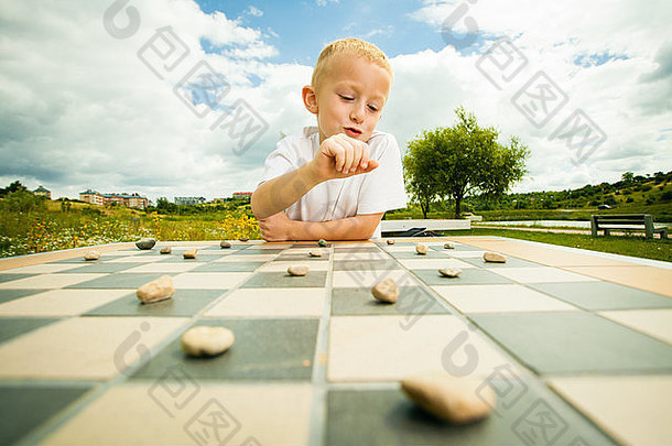 绘图板游戏。小男孩聪明的孩子玩跳棋思考，户外公园。儿童与发展