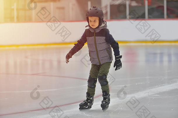 穿着冬衣，带着保护装置的可爱小男孩在溜冰场上滑冰