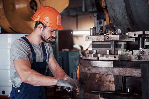一个戴着安全帽的年轻工人在一家大型金属厂的肖像。工程师为机器提供服务，并为气体设备制造零件