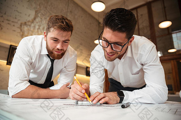 两个年轻兴奋的商人站在桌子边，手里拿着一张图，正在做一份商业计划书