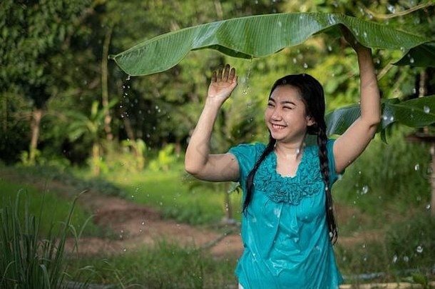 绿色花园背景下，一位留着黑发的亚洲年轻女子手持一片香蕉叶的肖像