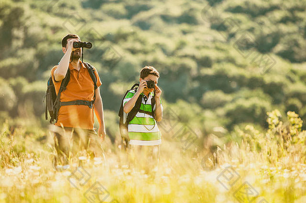 父亲和儿子夏天在大自然中徒步旅行。那个男孩正在拍照。