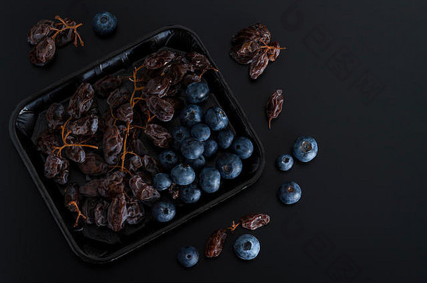 在黑色背景上分离的托盘上放着一串干燥的苏丹娜和蓝色浆果