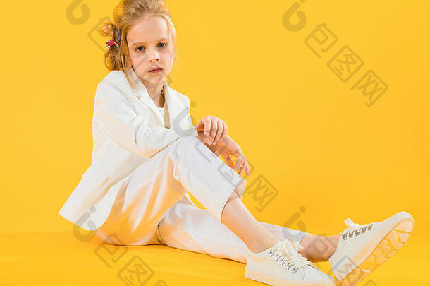 十几岁的女孩白色衣服坐在伸展运动腿向前黄色的背景