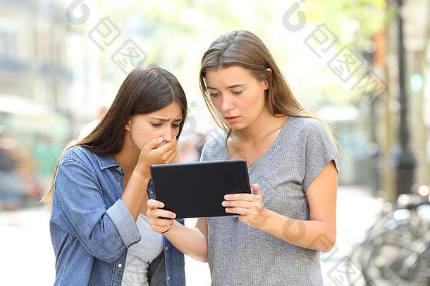 两位忧心忡忡的朋友在街上的平板电脑上阅读在线新闻