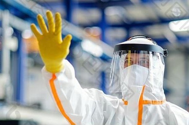 在工业工厂，工人戴着防护面罩和防护服，打招呼手势。