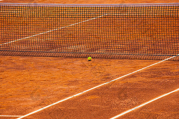 一个空网球场的股票图像，网和黄色的球靠近它。这是一个晴朗的日子，球场在比赛前就准备好了