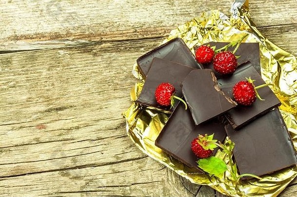 在木板上用<strong>金箔纸</strong>包裹的苦巧克力。巧克力美味。野生草莓