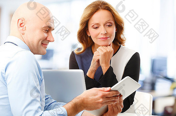 高级商人手持数字平板电脑，与成熟的女商人讨论问题。