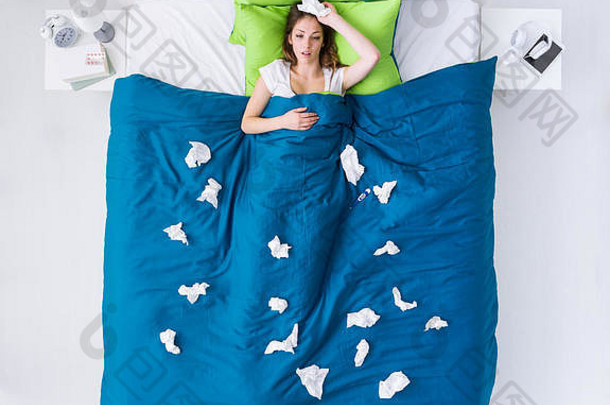 顶视图：一位患有流感病毒的悲伤妇女躺在家里的床上，周围都是组织