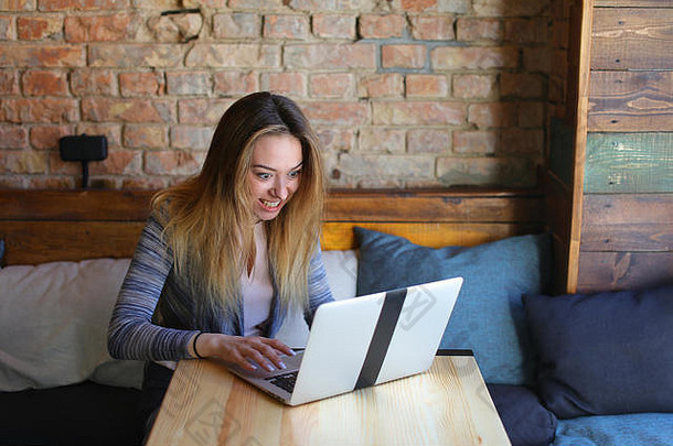 一位女士坐在桌子旁舒适的咖啡馆里，端着一杯咖啡，用笔记本电脑进行交流。