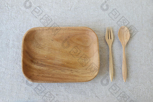 亚麻布桌子背景上的带勺子和叉子的空木盘